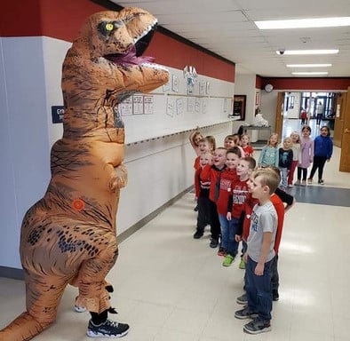elementary students in hallway with teacher dressed in an inflatable T-Rex costume
